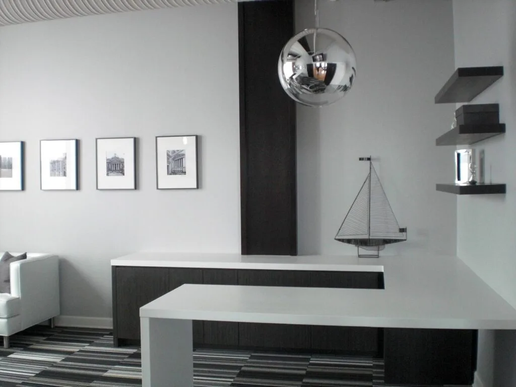 Modern trading office interior with minimalist executive workspace featuring white desk surfaces dark wood cabinetry floating shelves and contemporary pendant lighting in a loft-style office design